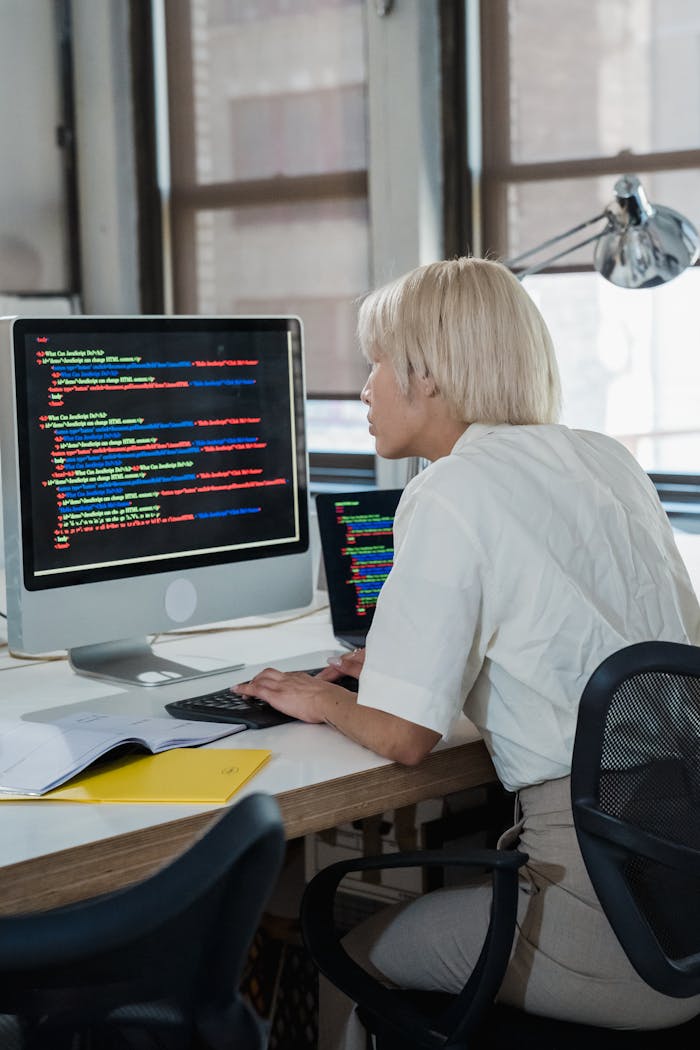 Woman engaged in software programming in a contemporary office setting with multiple screens.